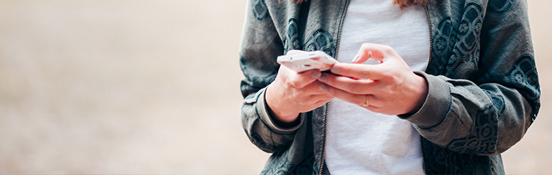 Eine Person in Freizeitkleidung bedient ihr Smartphone mit beiden Händen im Freien.