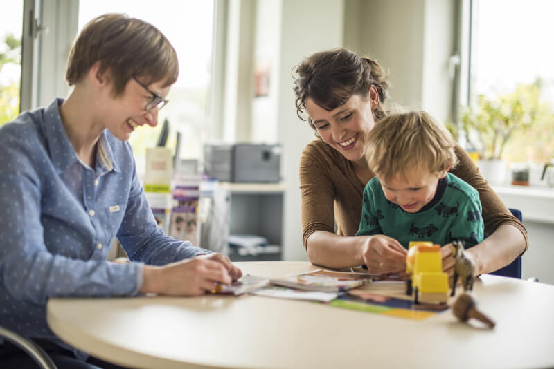 Zwei Frauen und ein Kind an einem Beratungstisch, während sie gemeinsam spielen und lachen