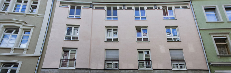 Schlichtes Wohnheim mit hellbeiger Fassade und symmetrisch angeordneten Fenstern zwischen zwei Altbauten