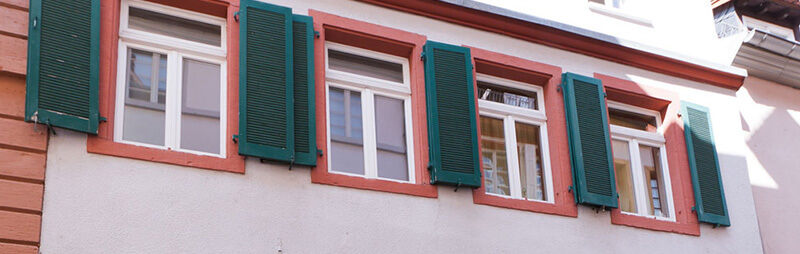 Wohnheimfassade mit weißen Fenstern und grünen Fensterläden in traditioneller Altstadtarchitektur