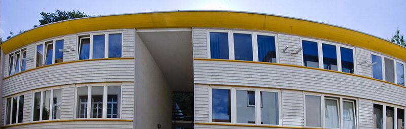 Flachbau mit abgerundeter gelber Dachkante und großflächigen weißen Holzpaneelen und Fenstern