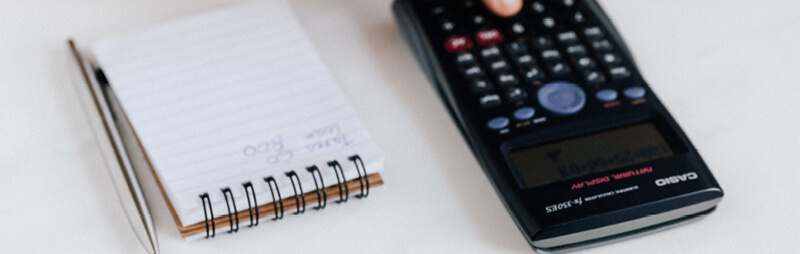 Ein wissenschaftlicher Taschenrechner neben einem Notizblock mit einer Liste und einem Kugelschreiber.