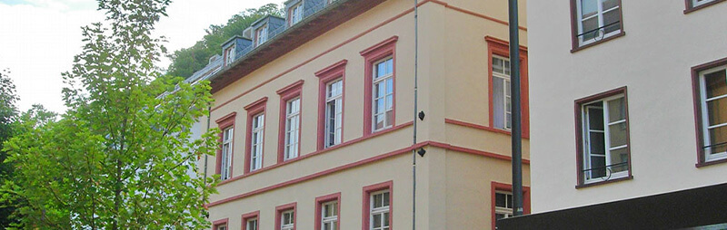 Dreistöckiges Wohnheim mit gelber Fassade und roten Fensterrahmen, flankiert von modernen Nachbargebäuden