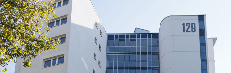 Hochhaus mit Glasfassade und runder Gebäudeecke, auf der die Nummer „129“ groß zu sehen ist