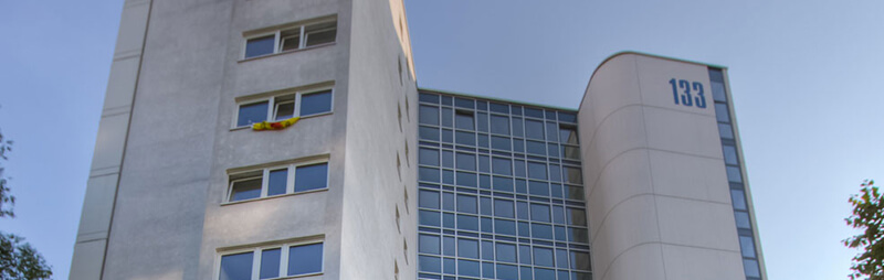 Modernes Hochhaus mit weißer Fassade, großflächiger Glasfront auf der rechten Seite und deutlich sichtbarer Hausnummer „133“