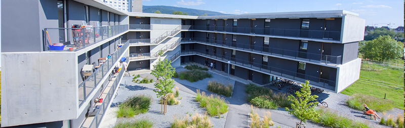 U-förmig angelegtes Wohnheim mit vier Stockwerken, offenen Gängen und begrüntem Innenhof mit Wegen