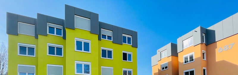 Zwei moderne Wohnheime in Grün und Orange mit grauen Akzentbereichen unter blauem Himmel