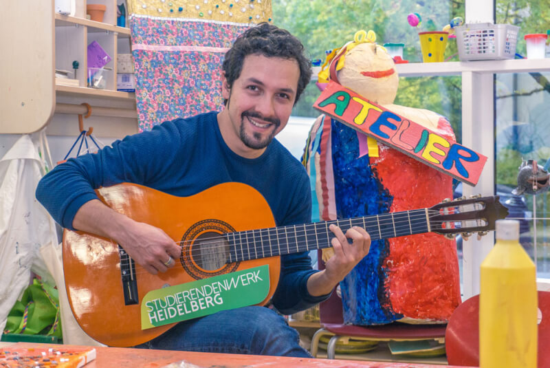 Mann mit Gitarre im farbenfrohen Kinderatelier des Studierendenwerks Heidelberg