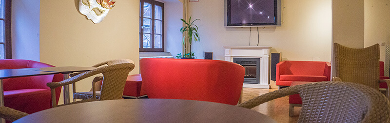 Gemütlicher Aufenthaltsraum mit roten Sesseln, Rattanstühlen, einem Wandfernseher und dekorativem Kamin.