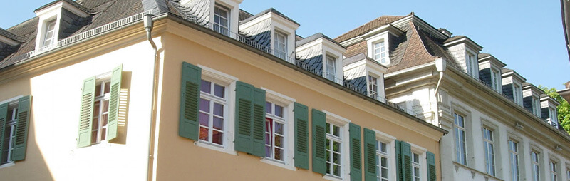 Historisches Wohngebäude mit hellem Anstrich, grünen Fensterläden und zahlreichen Gauben im Dachgeschoss