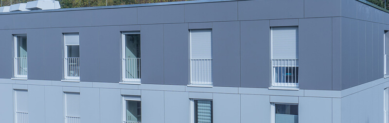 Ein modernes, grau-weißes Apartmentgebäude mit geschlossenen Fensterläden.