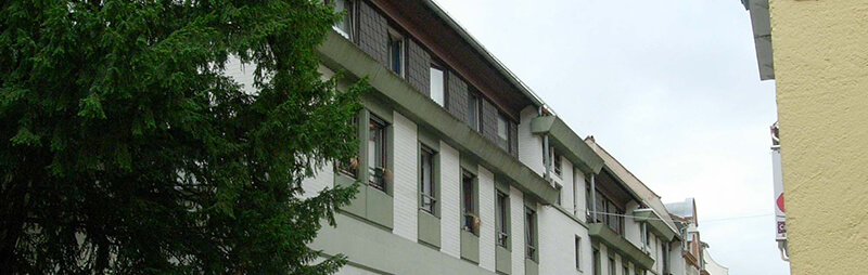 Langgestrecktes Altbauhaus mit klassischer Fassadengliederung und Fensterläden, von Bäumen flankiert