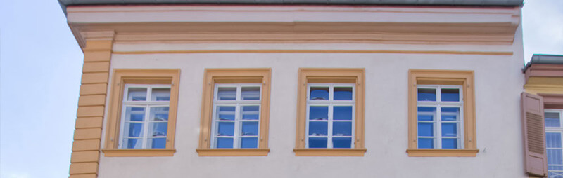 Klassizistisches Gebäude mit heller Fassade und orangefarbenen Fensterrahmen, schlicht und symmetrisch gegliedert