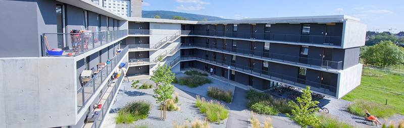 Eine moderne Wohnanlage in Betonoptik mit mehreren Etagen und Blick auf einen begrünten Innenhof.