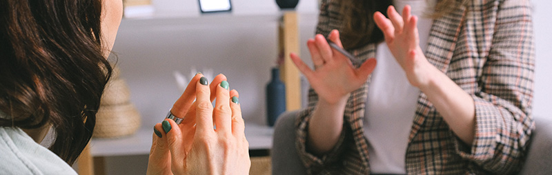 Zwei Personen sitzen sich gegenüber, tauschen sich aus und gestikulieren dabei mit den Händen. In einem gut beleuchteten Innenraum sind nur ihre Hände und ein Teil ihres Oberkörpers zu sehen.
