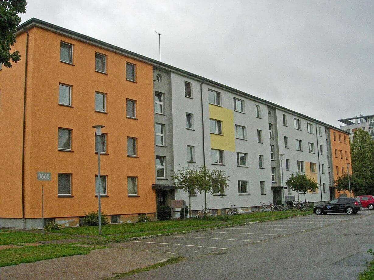 Student residence with four floors and a colorful facade mix of orange, gray and yellow; parking spaces and bicycle racks with bicycles parked in front.