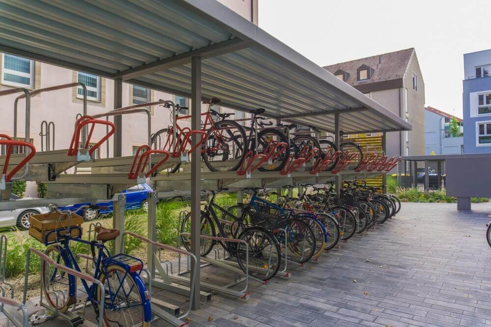 Überdachte, moderne Fahrradstellplätze mit doppelstöckigen Halterungen, teilweise belegten Stellplätzen und umliegender Begrünung im Innenhofbereich.