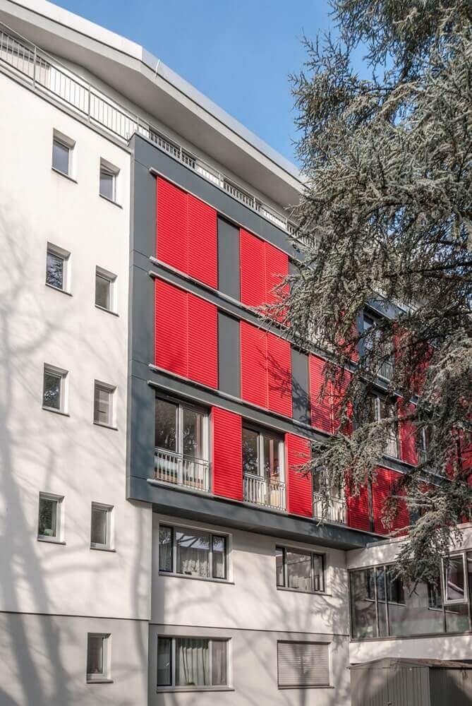 Moderne Außenfassade des Studentenwohnheims mit roten Klappläden und kleinen Balkonen in ruhiger Lage.