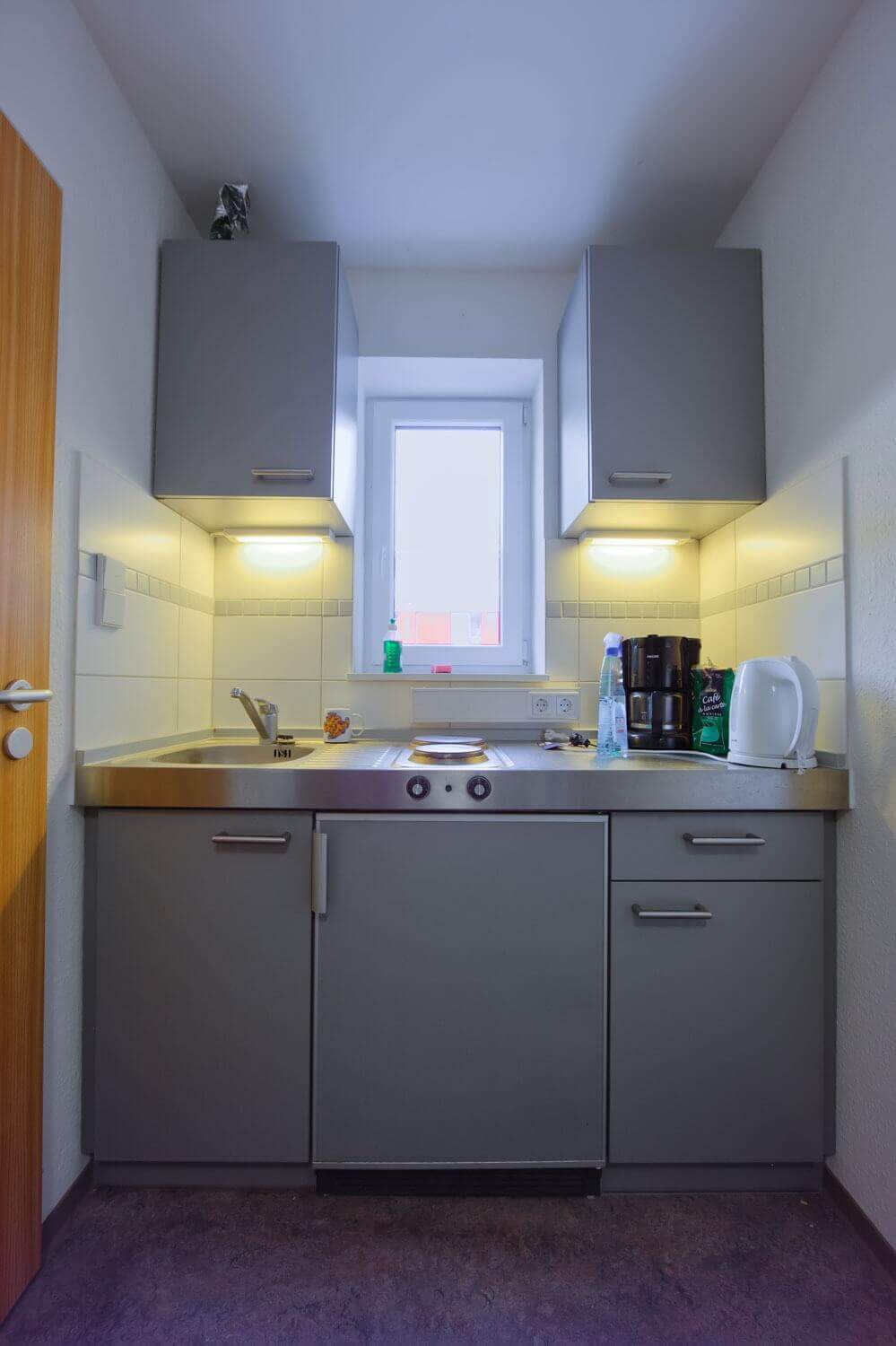 Kompakte Küchenzeile mit Spüle, Herdplatte und Oberschränken in einem der Appartements im Studentenwohnheim.