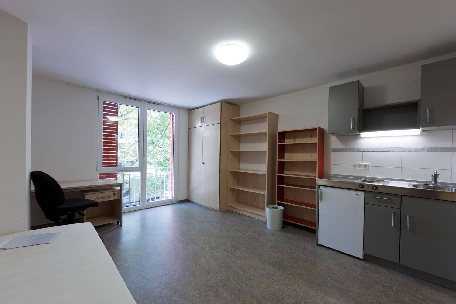 Einzelappartement im Studentenwohnheim mit großer Fensterfront, Küchenzeile, Schreibtisch und mehreren Schränken.