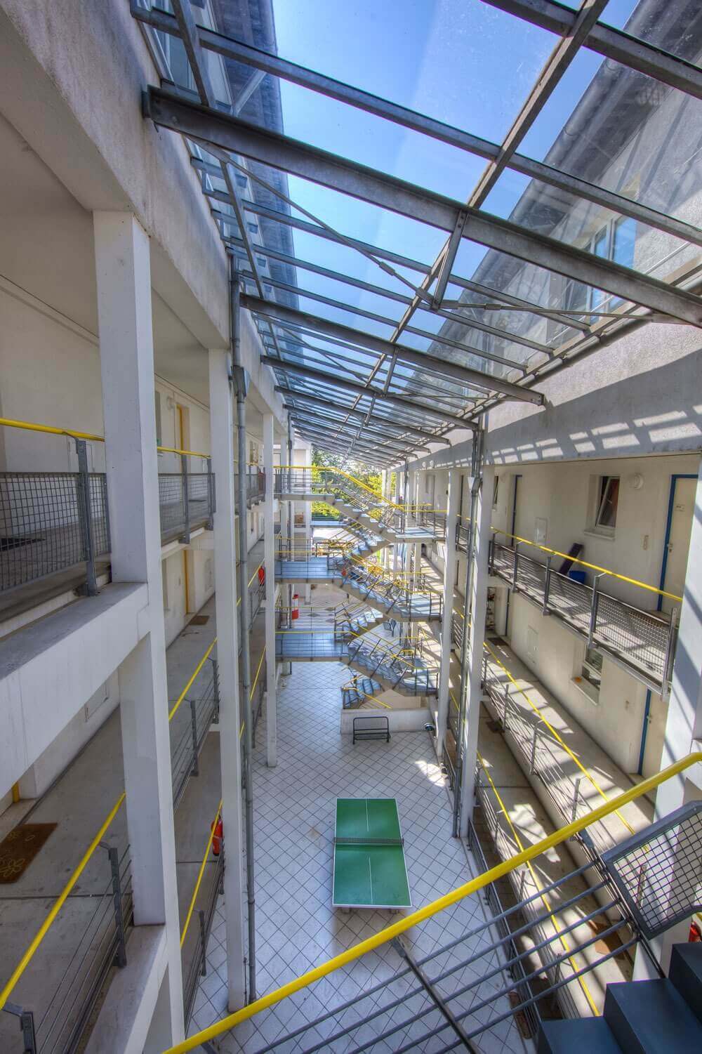 Weitläufiges, lichtdurchflutetes Atrium mit überdachten Laufstegen und Tischtennisplatte im Innenbereich des Studentenwohnheims