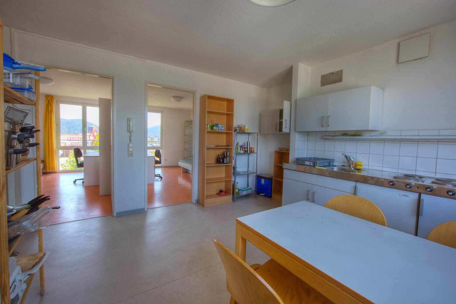 Gemeinschaftsküche mit Blick auf zwei benachbarte Zimmer, großzügigem Essbereich und offener Regalstruktur