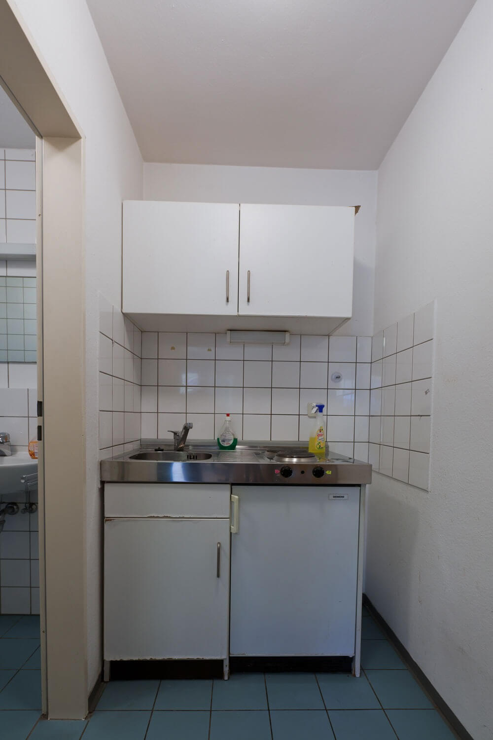 Ansicht einer kleinen Küchenzeile mit Kochfeld, Spüle, Hängeschrank und Putzutensilien, typisches Erscheinungsbild eines Studentenappartements.