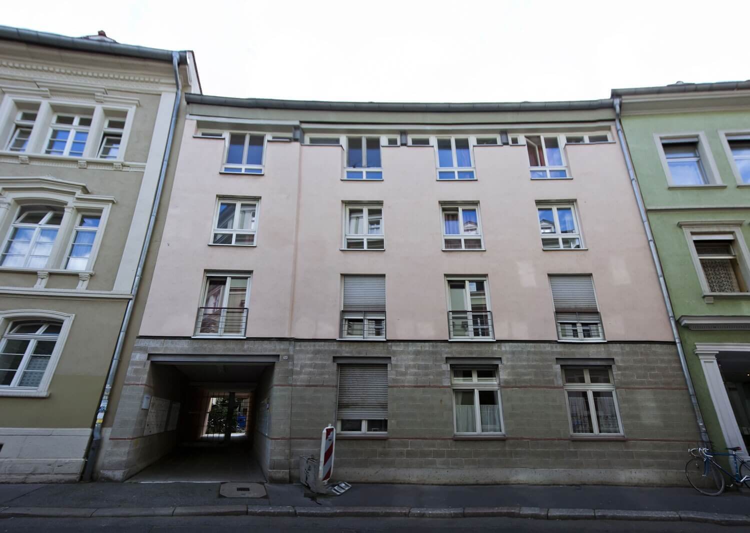 Außenfassade des Europahauses 3 in beige-grauer Farbgestaltung mit mehreren Fenstern, kleinem Torbogen zum Innenhof und umliegenden Altbauten.