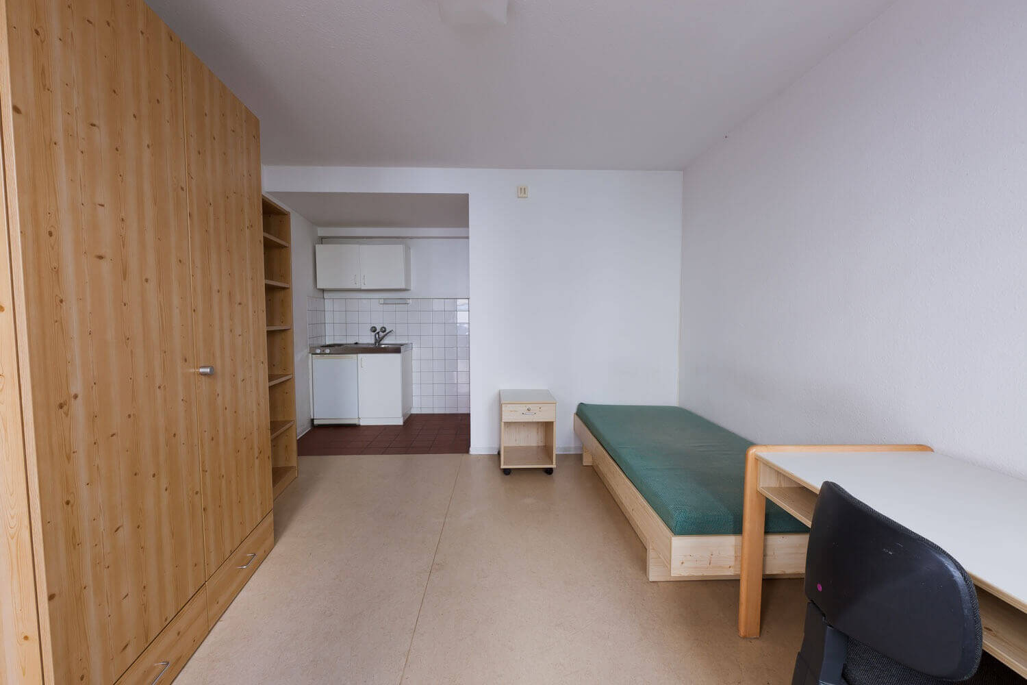 Einzimmerapartment im Europahaus 5 mit Bett, Schreibtisch, Kleiderschrank und Zugang zur offenen Kochnische im Hintergrund.