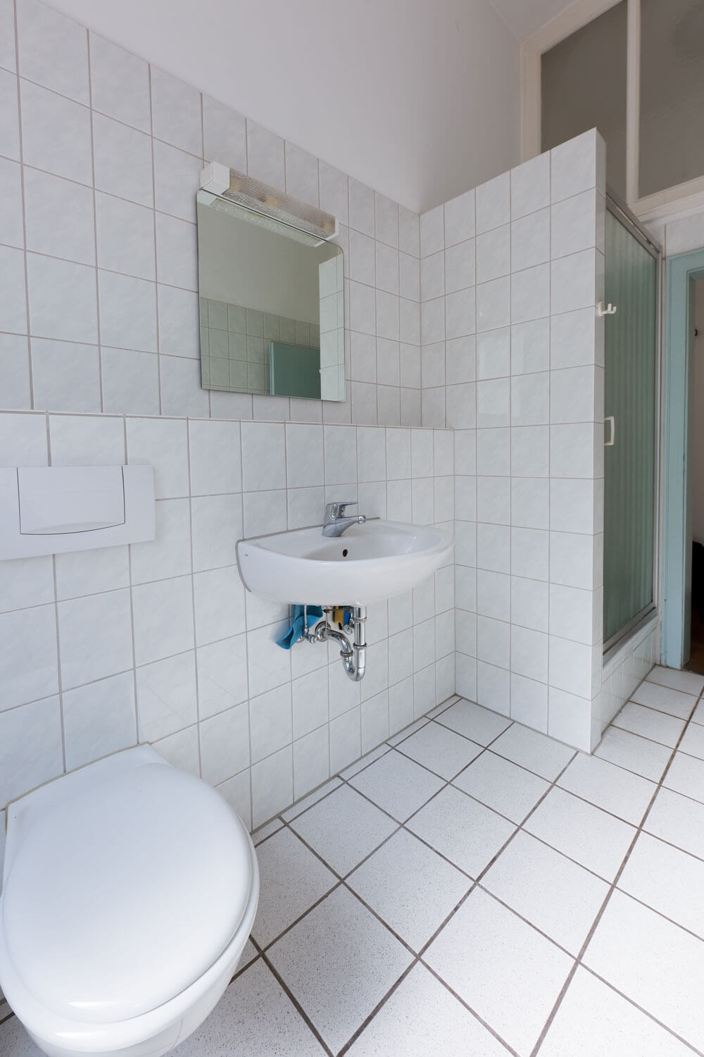 Modernes Badezimmer mit weißen Fliesen, WC, Wandspiegel, Waschbecken und Duschkabine.