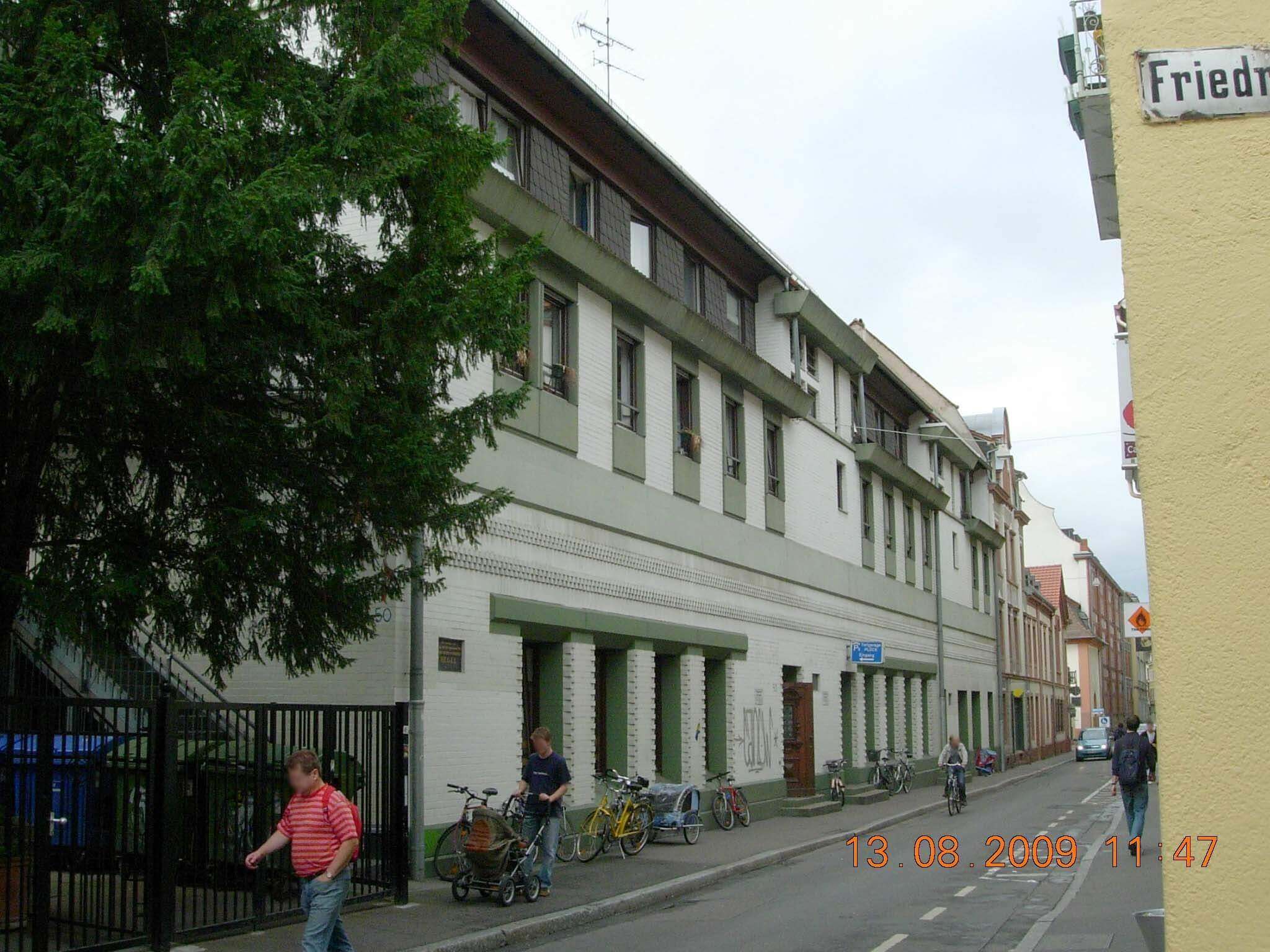 Straßenansicht eines Studentenwohnheims mit weißen Ziegelwänden und grünen Akzenten, mehreren Etagen und Fahrrädern entlang des Gehwegs.