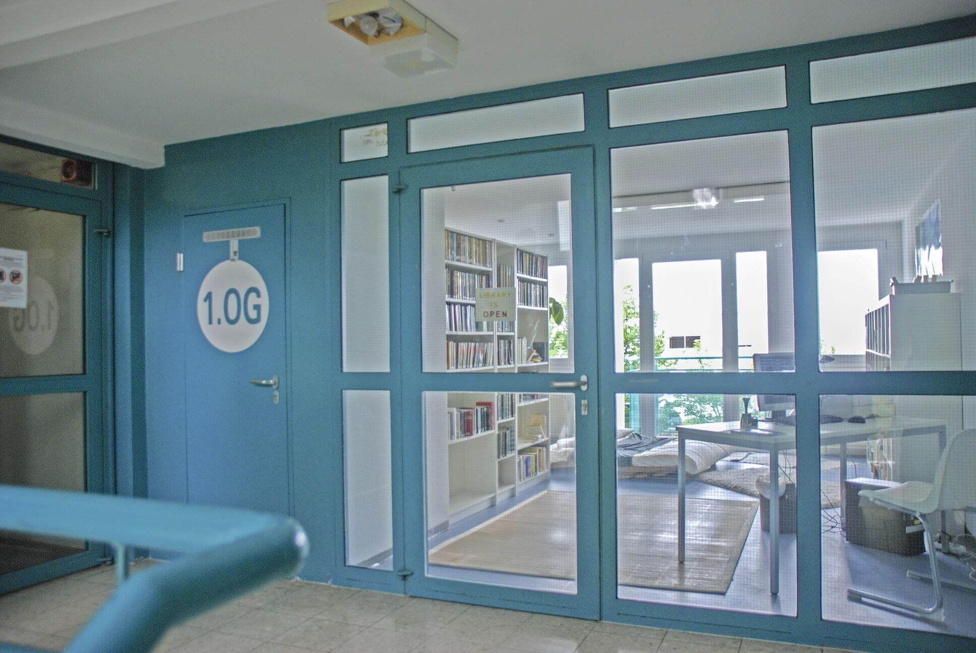 Hallway overlooking a common room or library with glass doors, books and seating.