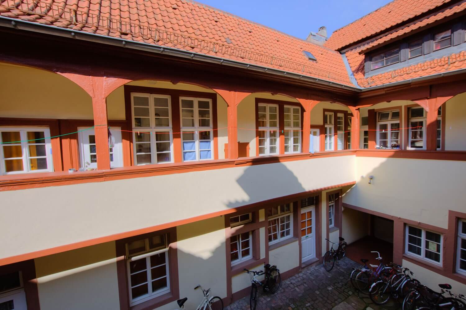 Blick von oben auf einen Innenhof mit hellen Hausfassaden, roten Fensterrahmen und mehreren abgestellten Fahrrädern.