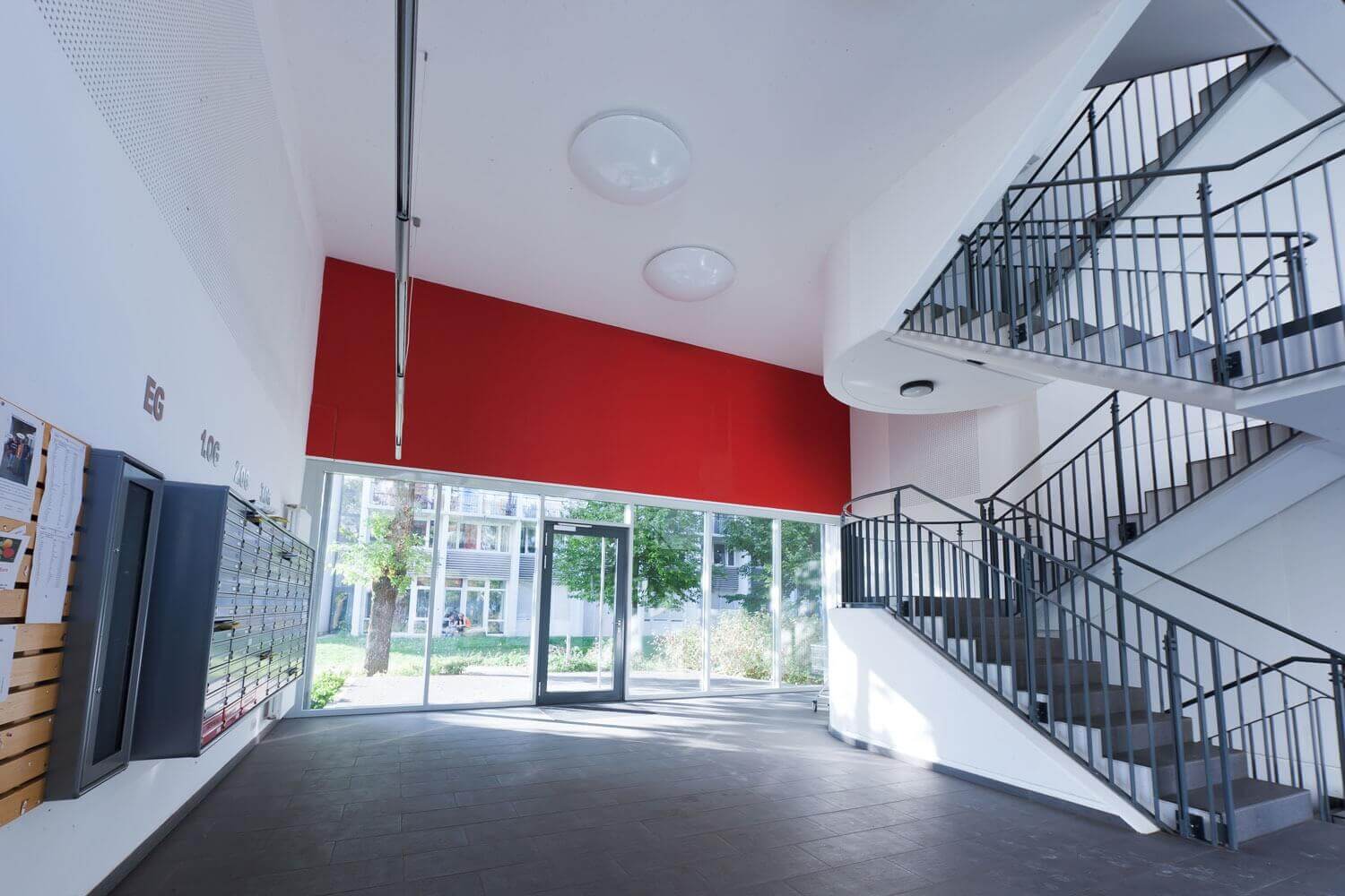 Großzügiger Eingangsbereich mit Briefkastenanlage, breiter Fensterfront und einer zweiläufigen Metalltreppe in einem Studentenwohnheim