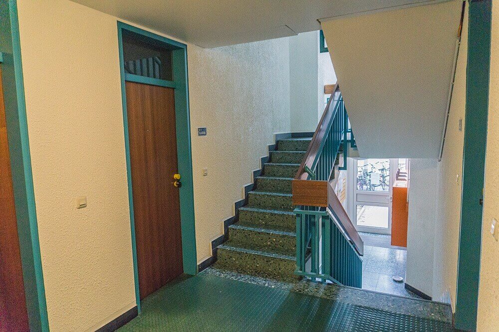 Treppenhaus im Studentenwohnheim mit türkisfarbenem Geländer, Gummiboden und Holztüren.