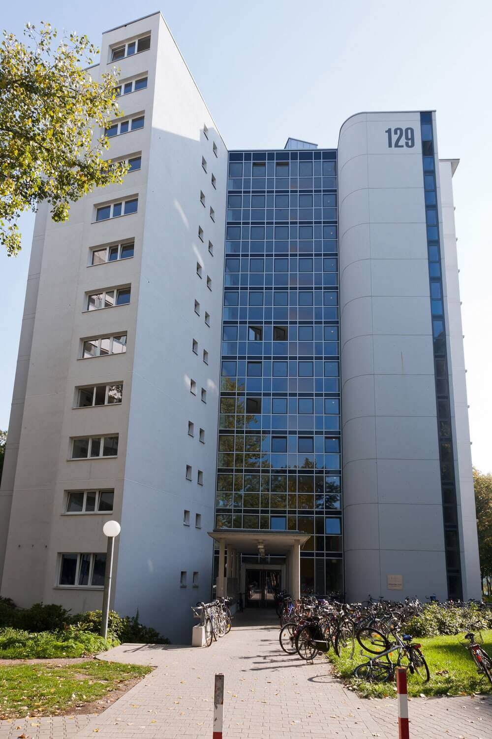 Mehrstöckiges Studentenwohnheim mit der Hausnummer 129, umgeben von Fahrrädern und Grünflächen, mit markanter Glasfassade.