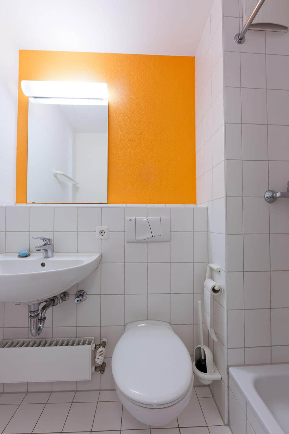 Modernes Badezimmer im Studentenwohnheim mit weiß gefliester Dusche, WC und Waschbecken sowie farblich akzentuierter Wand.