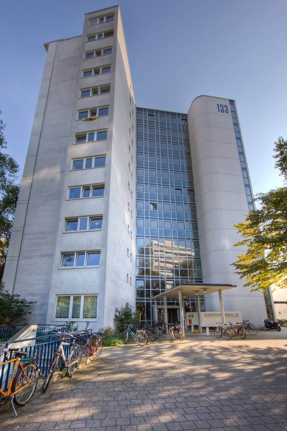 Frontansicht eines mehrstöckigen Studentenwohnheims mit der Hausnummer 133, großen Fensterfronten und zahlreichen abgestellten Fahrrädern am Eingang.