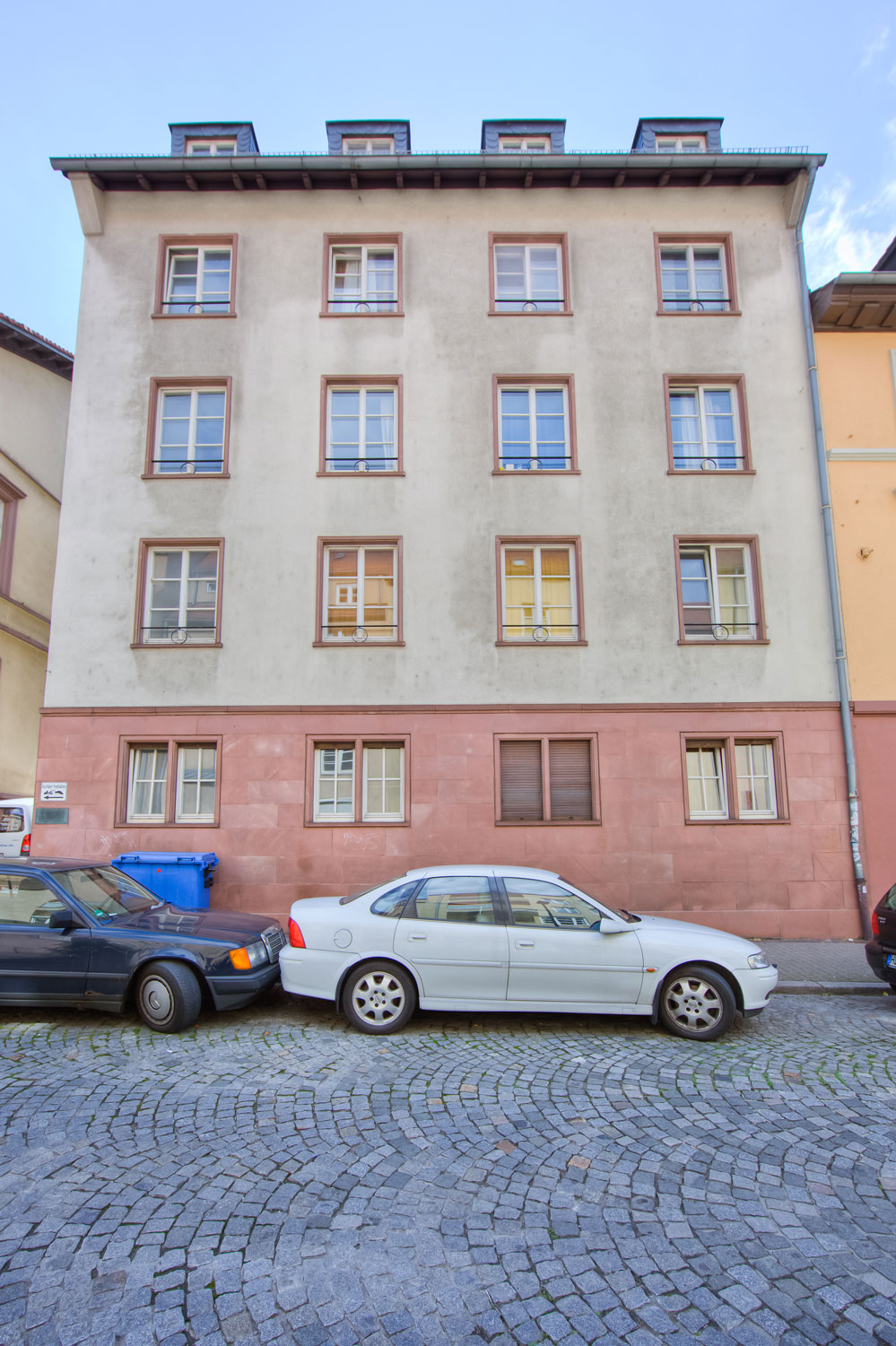 Außenansicht des Jellinekhauses mit hell gestrichener Fassade und mehreren symmetrisch angeordneten Fenstern; davor geparkte Autos auf einer gepflasterten Straße.