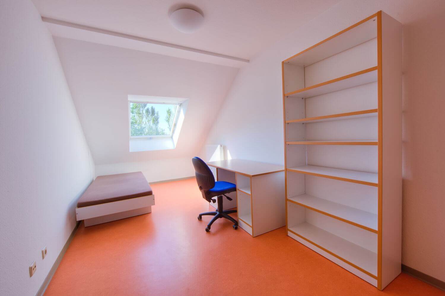 Bright attic room with bed, desk, swivel chair and shelving wall, daylight enters the room through an angled window