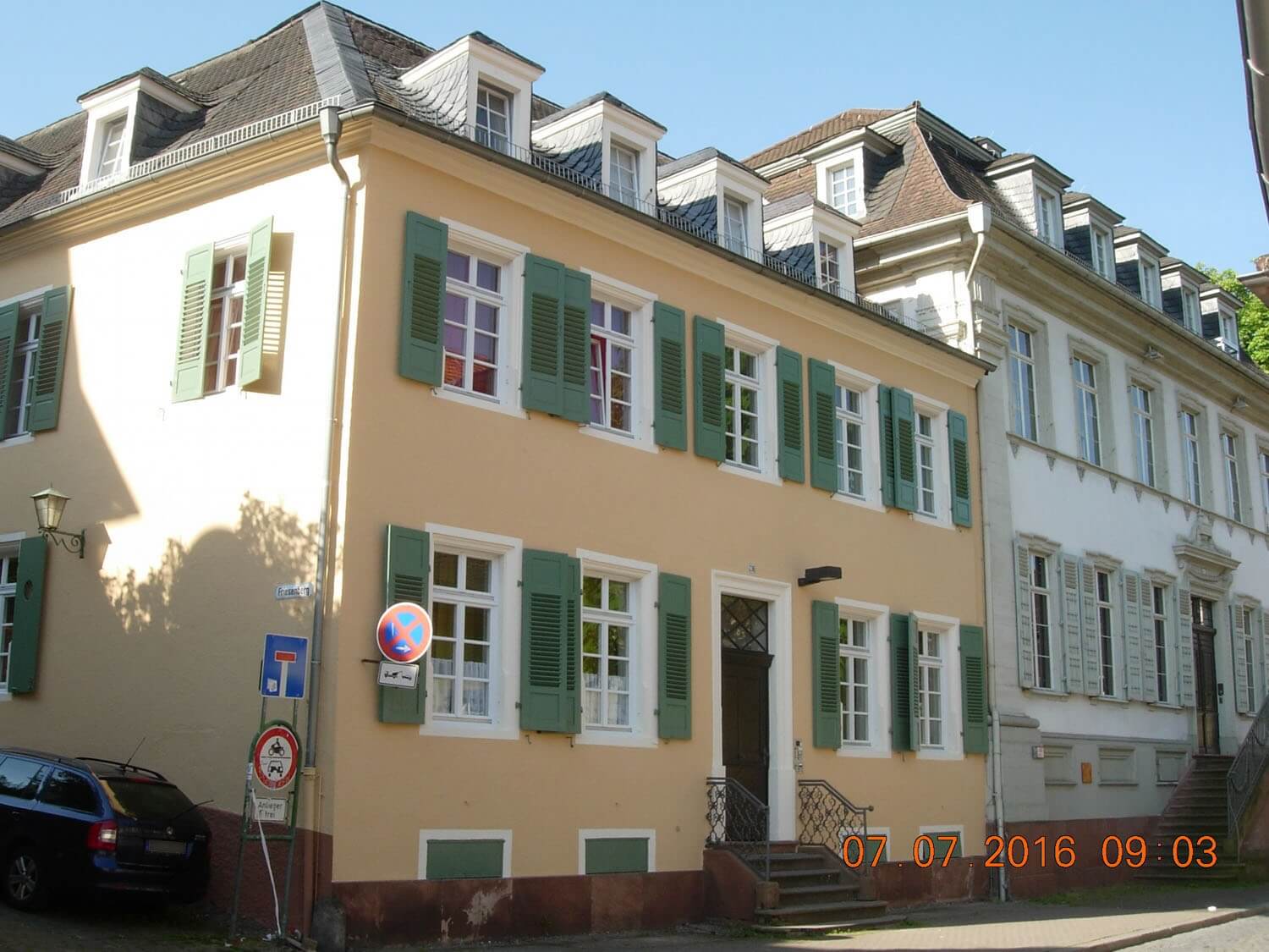 Außenansicht des Lieselottehauses mit hellgelber Fassade, grün gestrichenen Fensterläden und einem kleinen Treppenaufgang, gelegen in einer ruhigen Seitenstraße in der Altstadt.