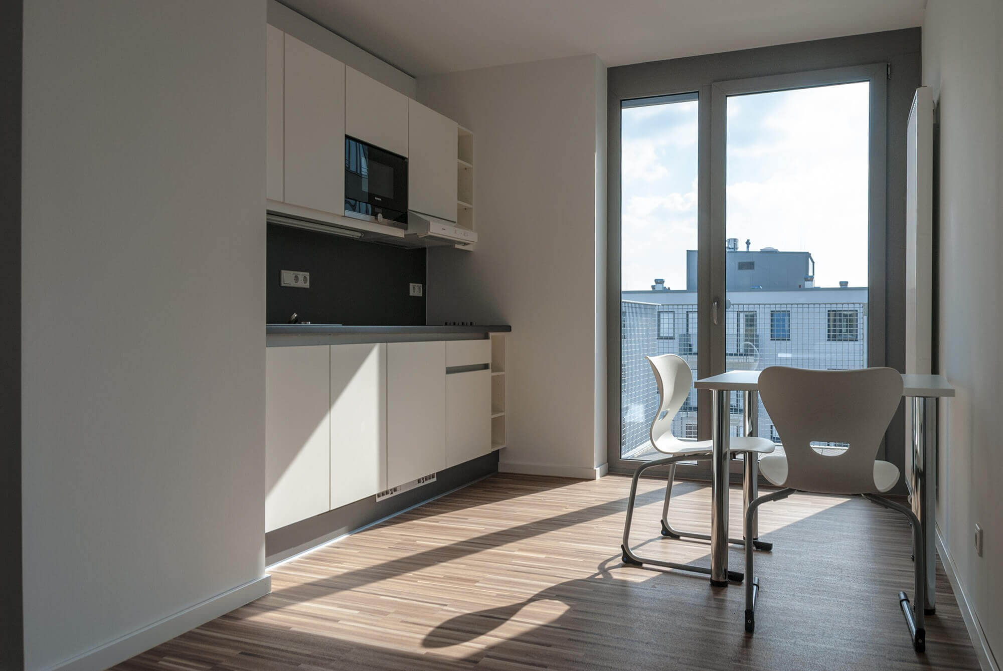 Modern communal kitchen with dining table in the student residence, large window front with view of neighboring buildings