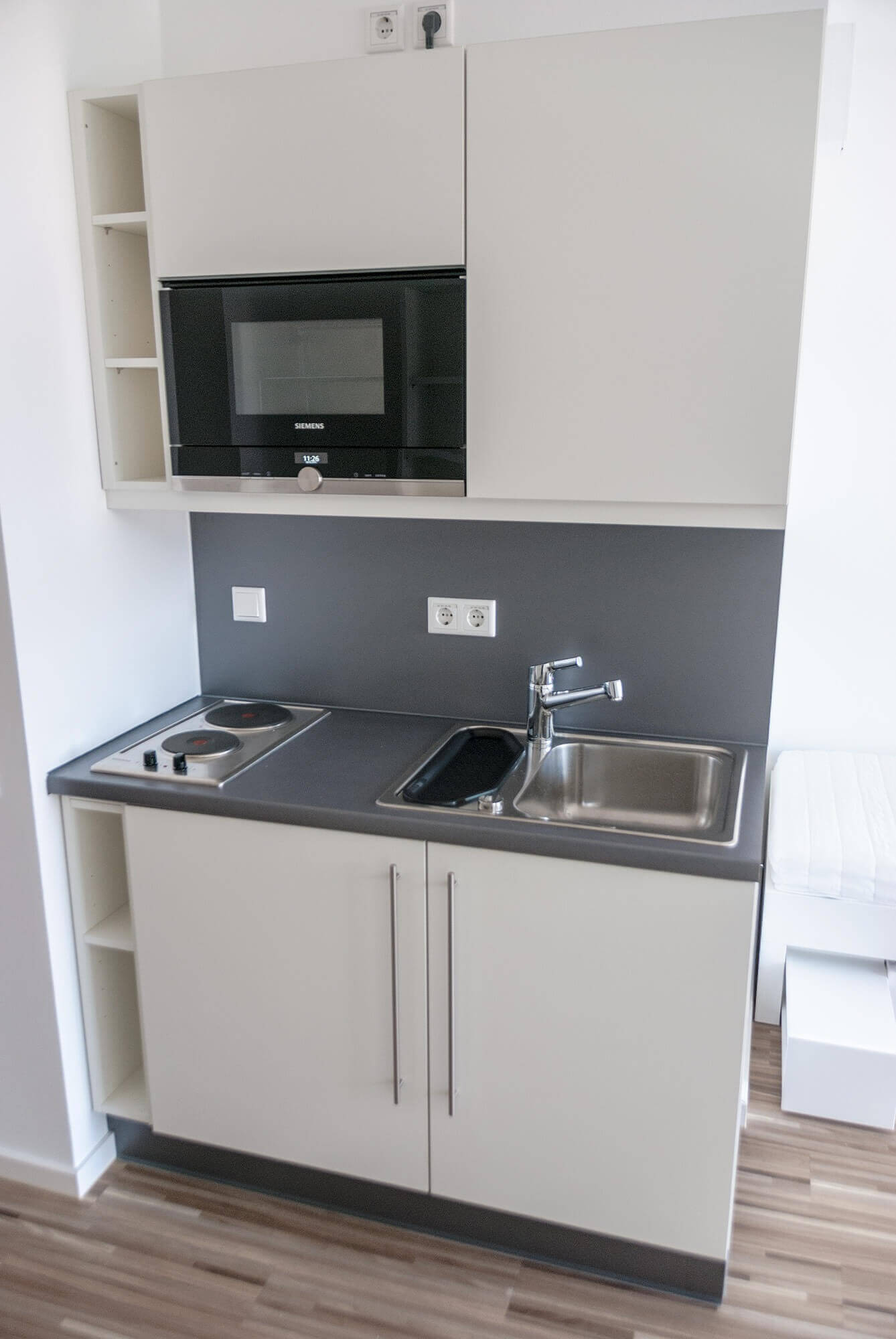 Compact kitchenette in student accommodation with two hobs, sink, wall units and microwave in a modern design.