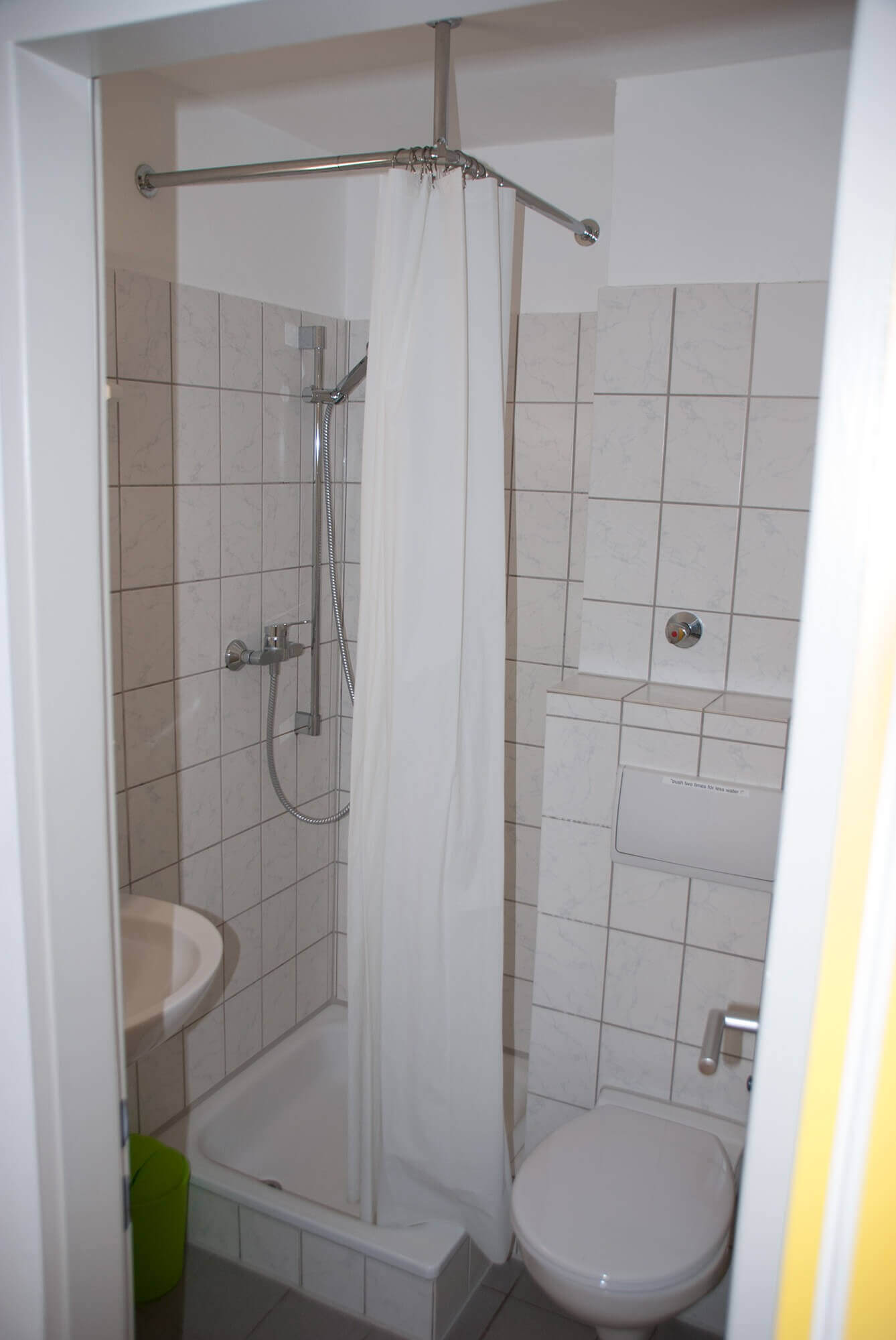 Kleines Badezimmer mit Dusche, weißem Duschvorhang und WC, vollständig gefliest.