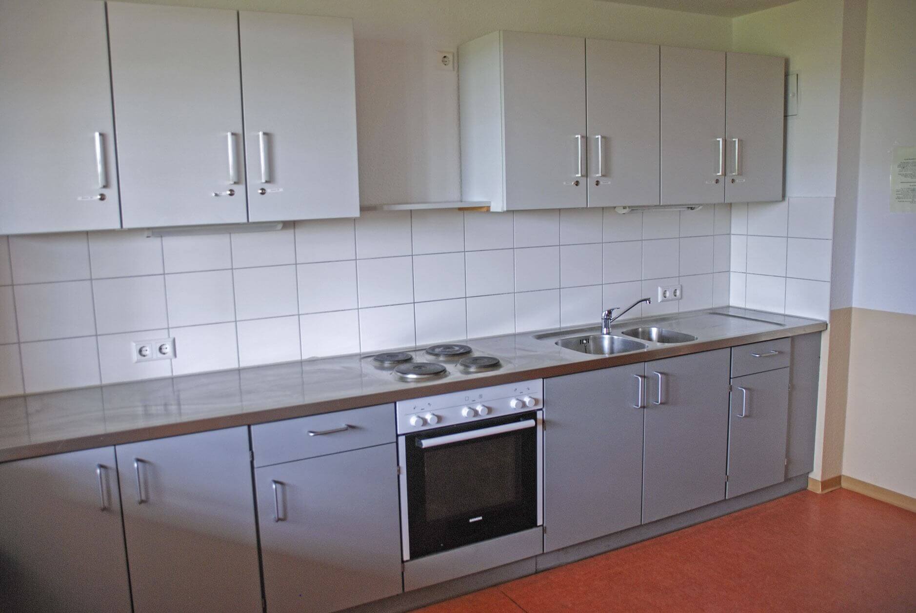 Moderne Gemeinschaftsküche mit weißen Oberschränken, Herd, Spüle und grauen Unterschränken.