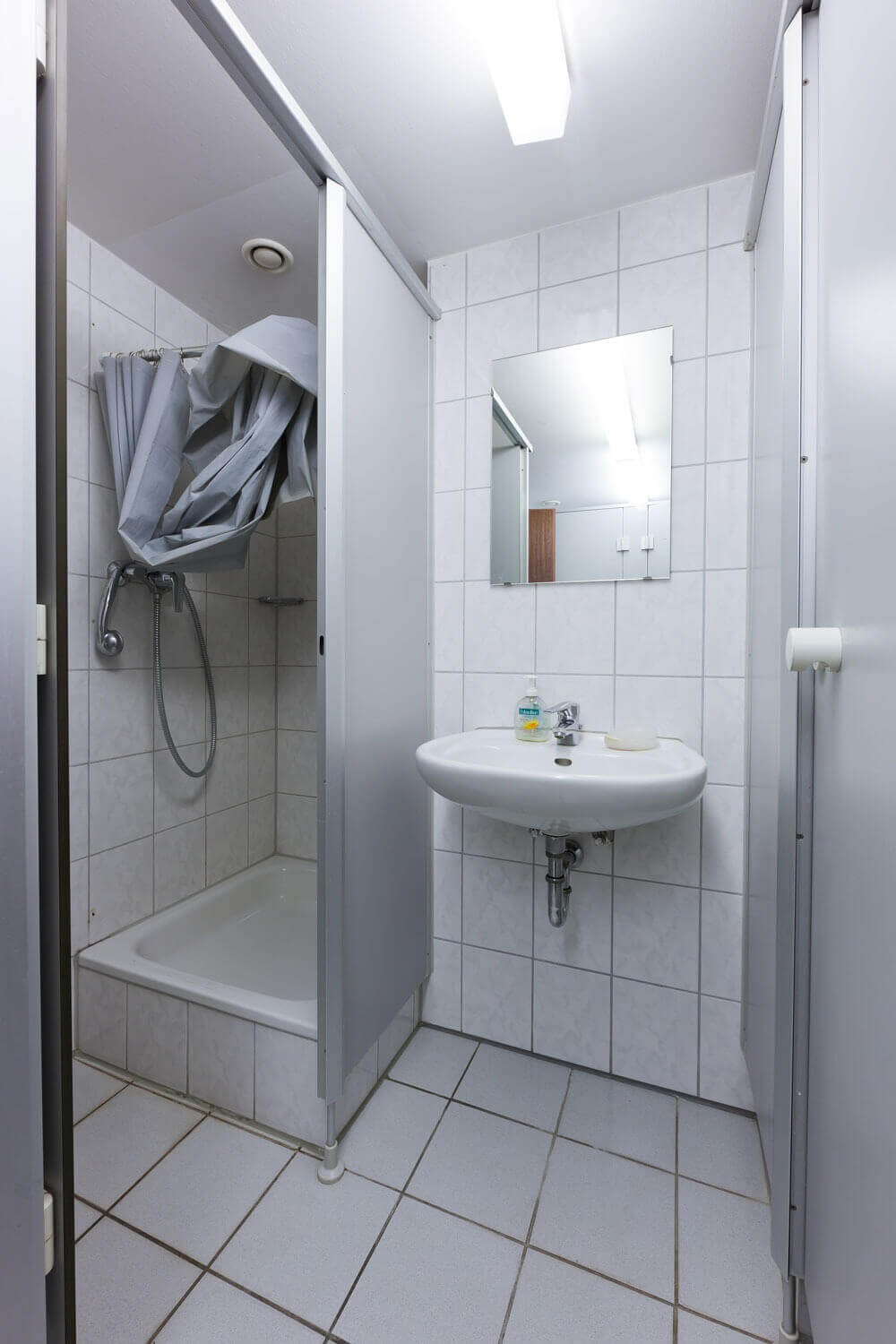 Duschkabine mit Vorhang, Waschbecken und Spiegel in einem gemeinschaftlich genutzten Badezimmer