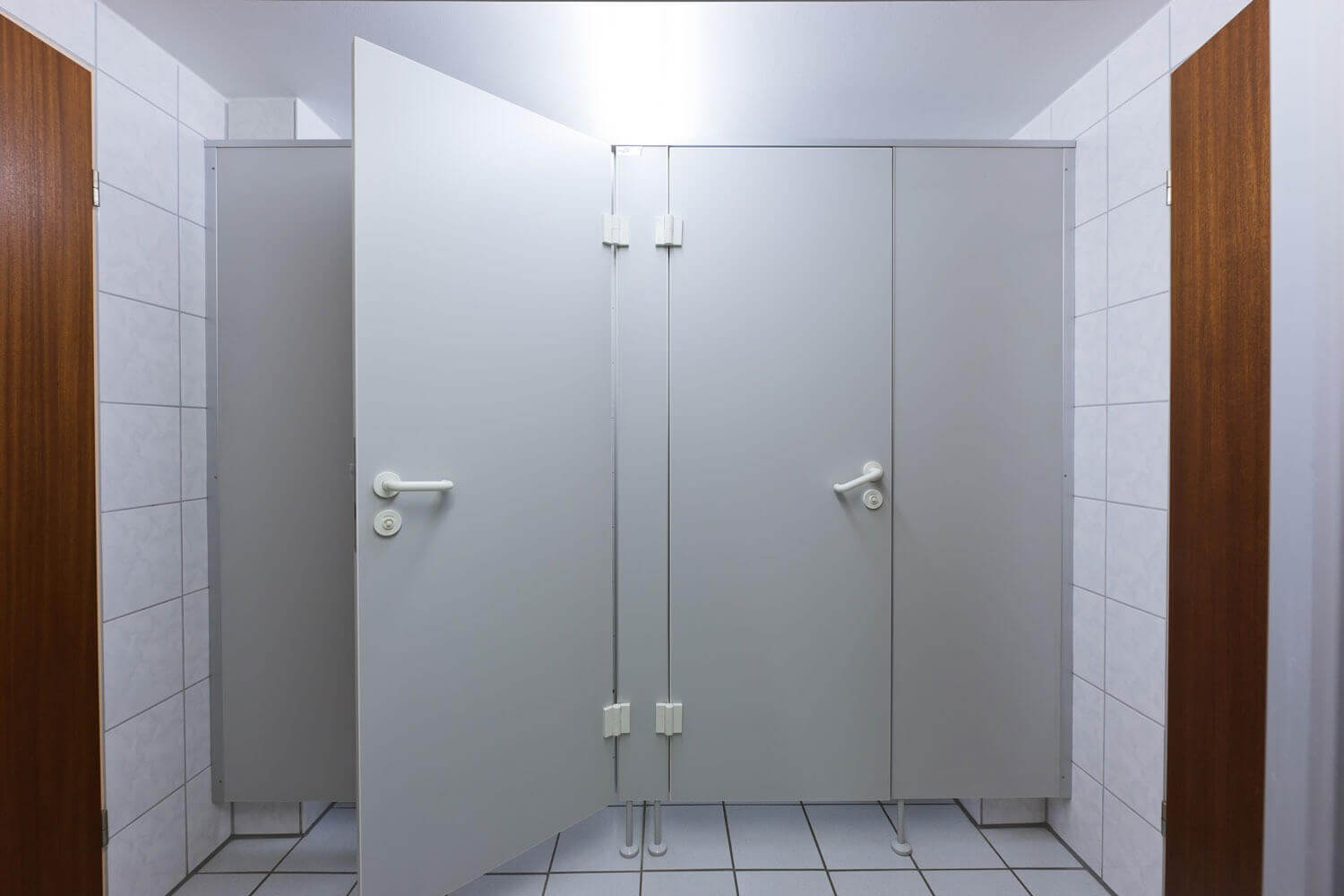 Mehrere verschlossene WC-Kabinen in einem hell gefliesten Gemeinschaftsbad