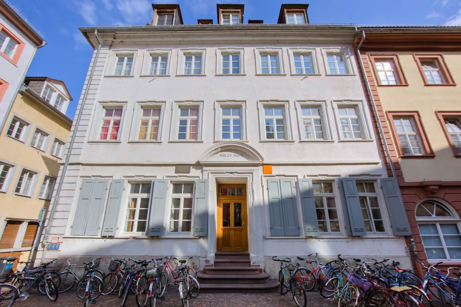 Außenansicht des historischen Sibley-Hauses mit heller Fassade, Holzfensterläden und zahlreichen Fahrrädern vor dem Eingang.