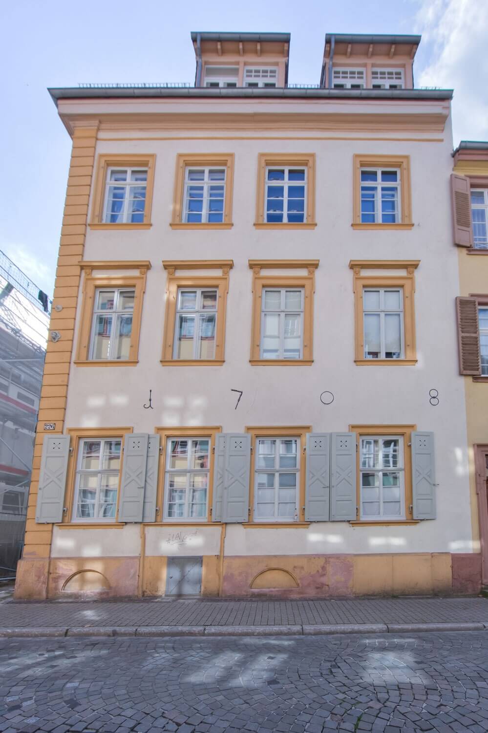 Frontansicht des Walpergenhauses mit symmetrisch angeordneten Fenstern, gelben Fensterrahmen und hellen Fensterläden im Erdgeschoss, davor Kopfsteinpflaster.